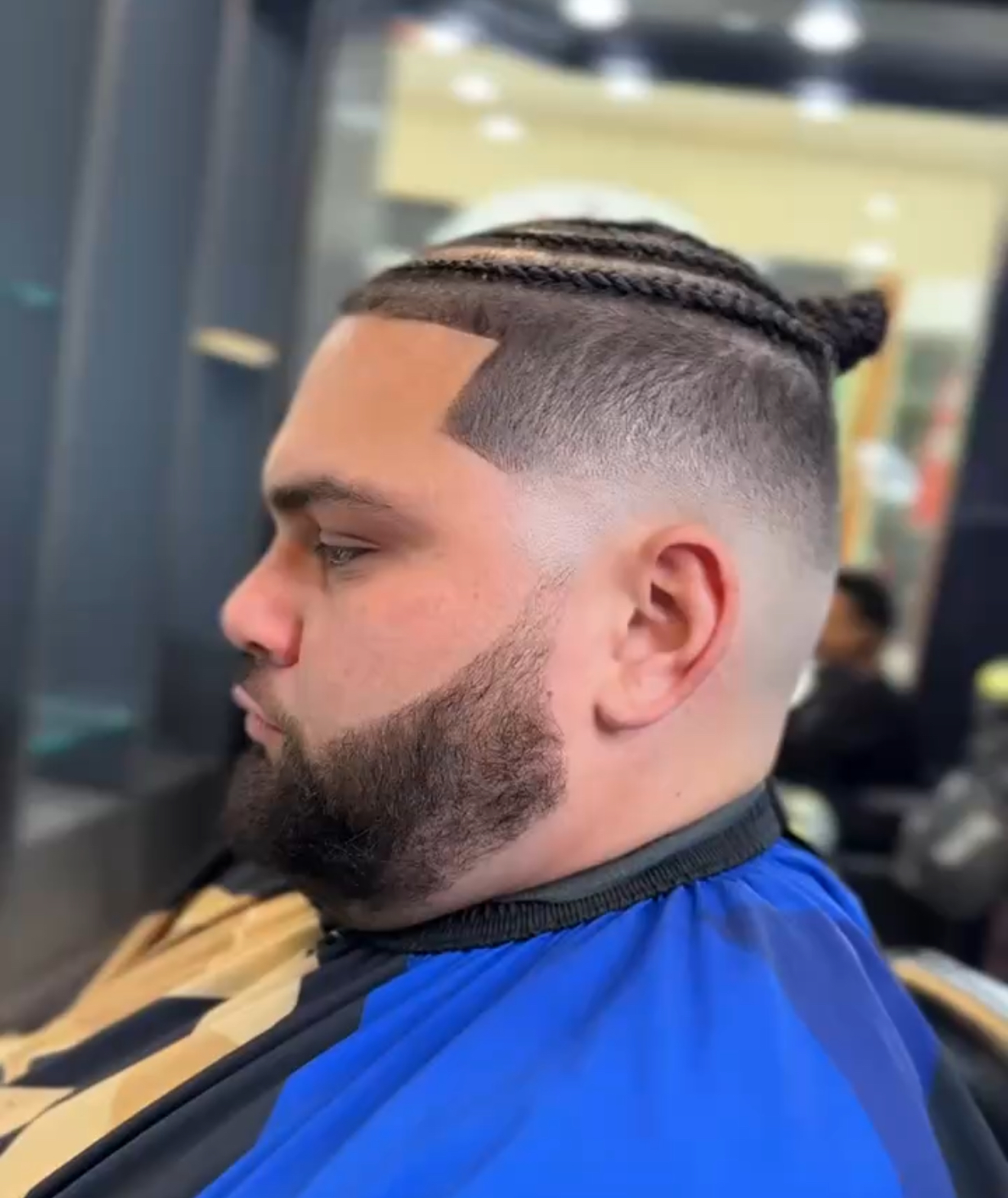 Mid fade with cornrows tied up top and a shaped beard